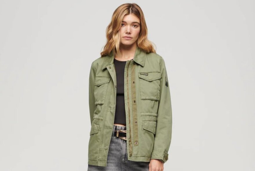 A model posing in a green army jacket with jeans and a tshirt.