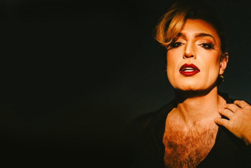 Drag performer wearing heavy makeup with bared chest and blond forelock.