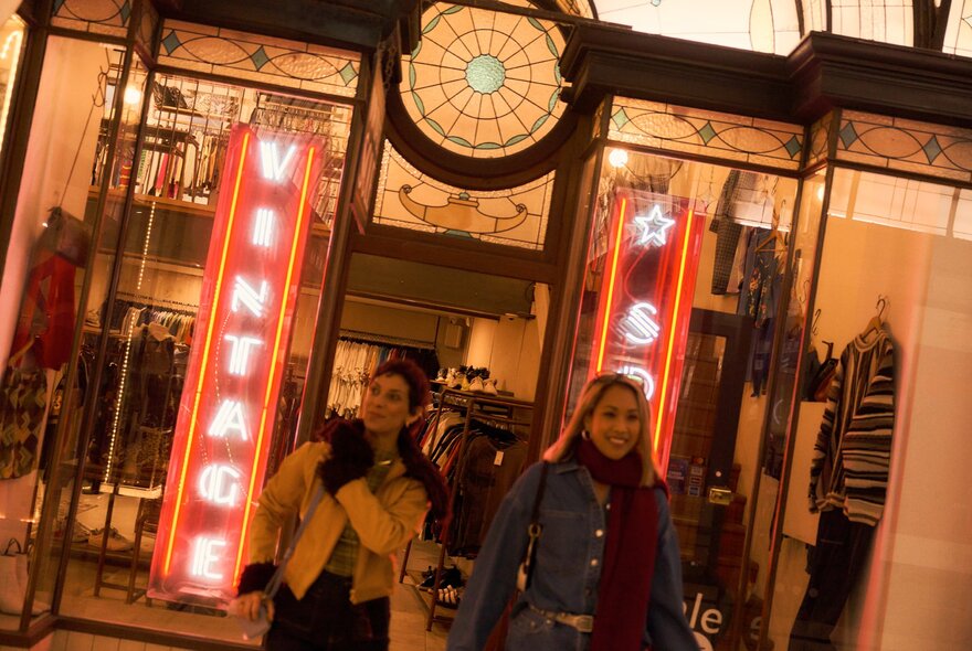 Two smiling friends, wrapped in winter scarves and wearing gloves, leaving the  clothing shop Vintage Sole located in the historic Cathedral Arcade in the Nicholas Building.