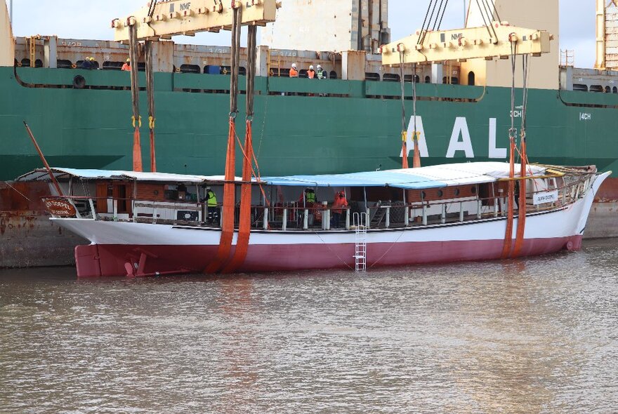 A boat being levered into place on the water at a dock with cranes.