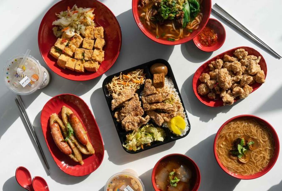 A bento box of fried chicken in the middle of a table of other fried food items.