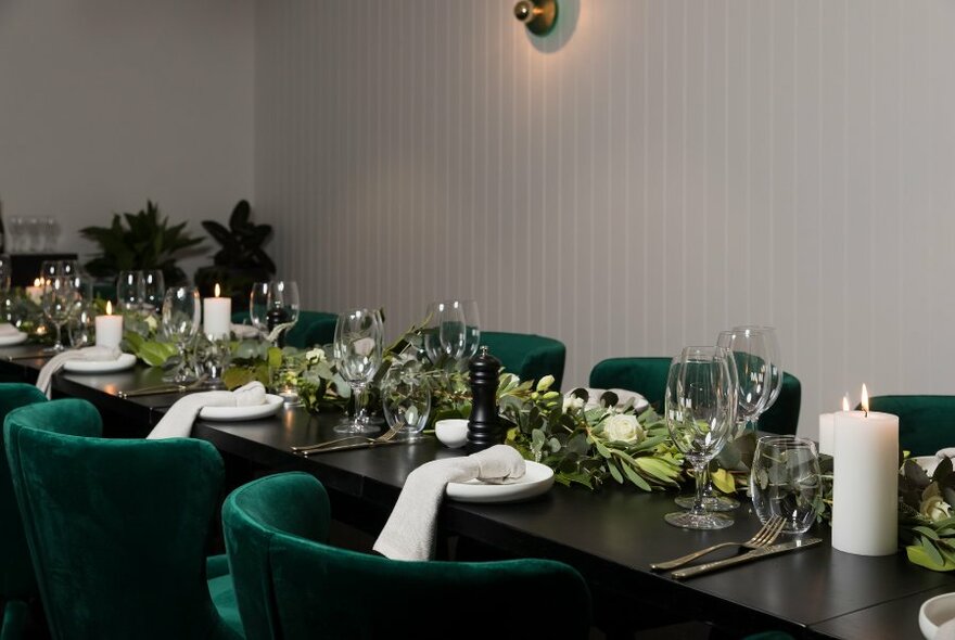 A black table set with floral arrangements and green velvet tub chairs