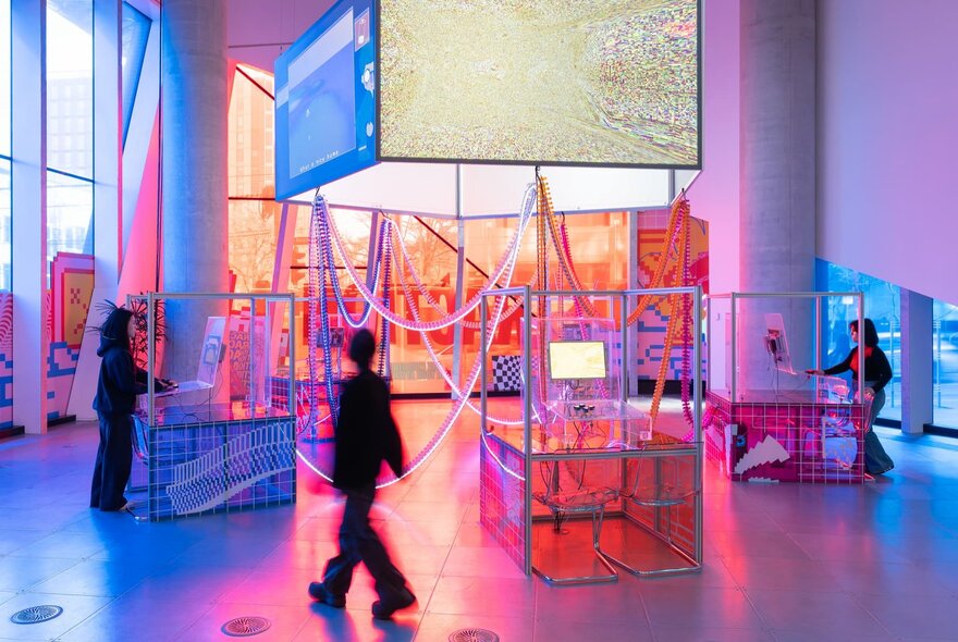 Three people interacting with a neon light installation in a gallery.
