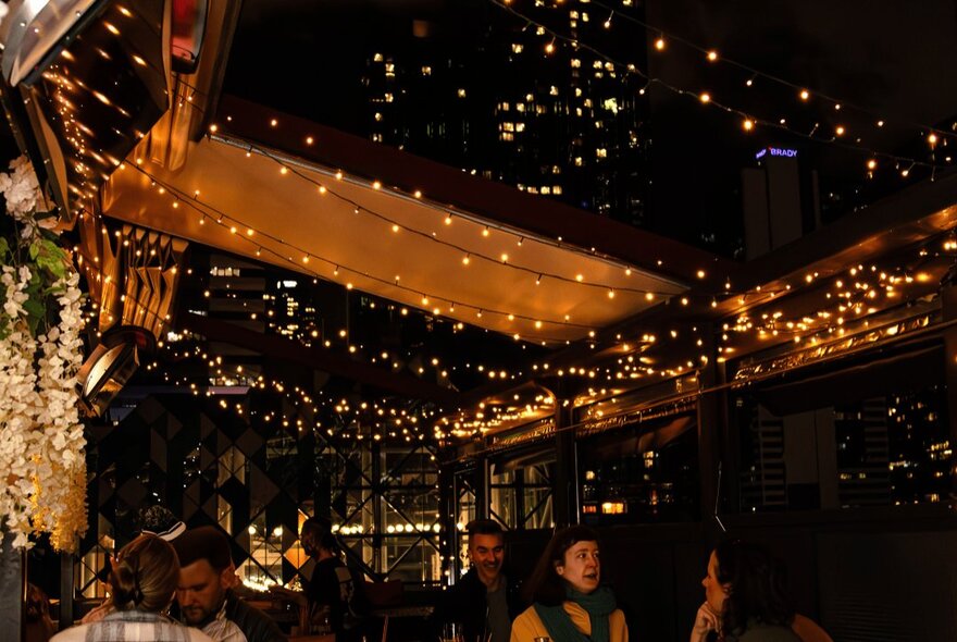 The rooftop open air bar at Goldilocks, decorated with twinkling fairy lights, some people socialising underneath the lights.