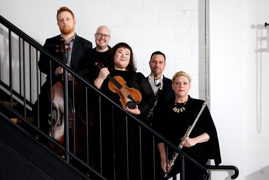 A group of musicians standing on a staircase holding instruments including a violin and flute.
