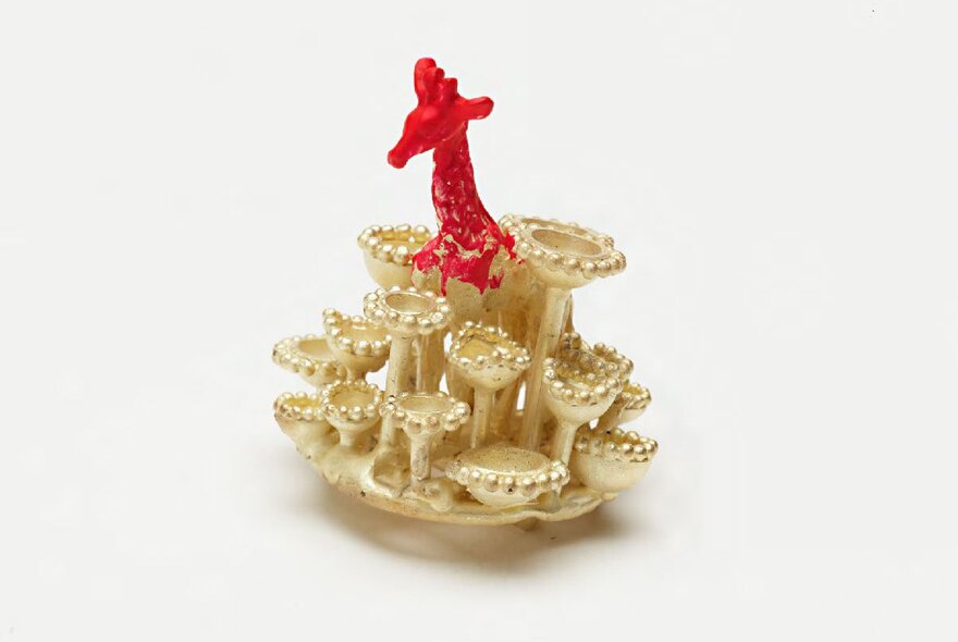 Intricate work of artist-jeweller Robert Baines in gold with a red figure on top.