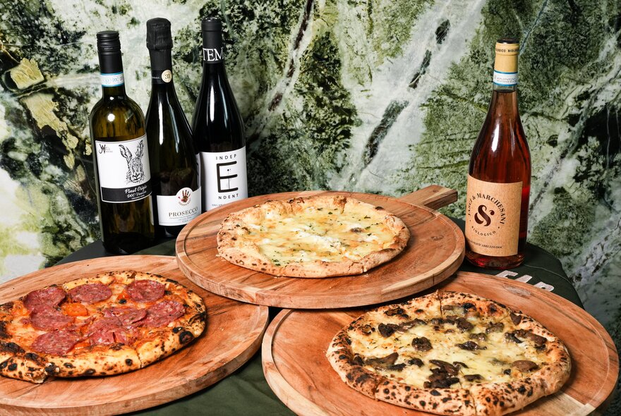 Three pizzas on individual round boards and four bottles of different wine. 