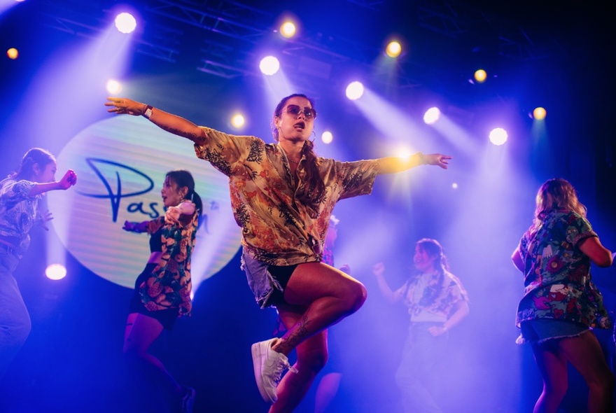 People spotlit and dancing on a stage, blue stage lights behind them. 