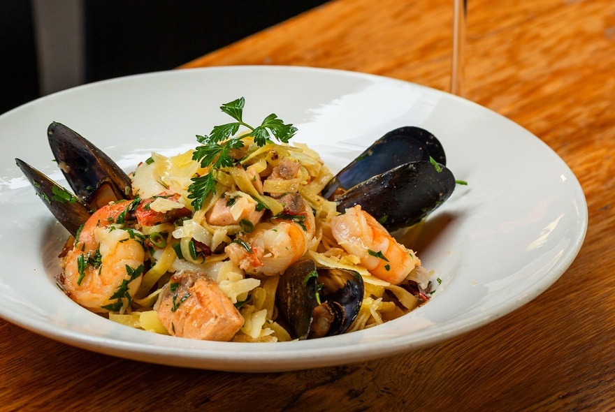 A white dish of pasta with prawns and mussels.