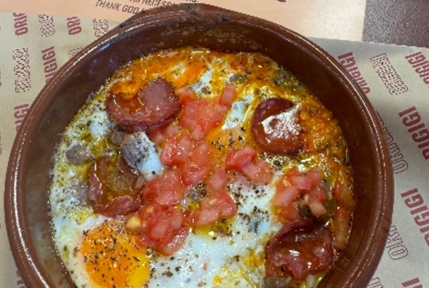 A terracotta dish of cooked eggs, sausage and tomato.