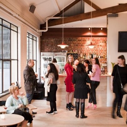 People seated and standing chatting in a bar area with pendant lights.