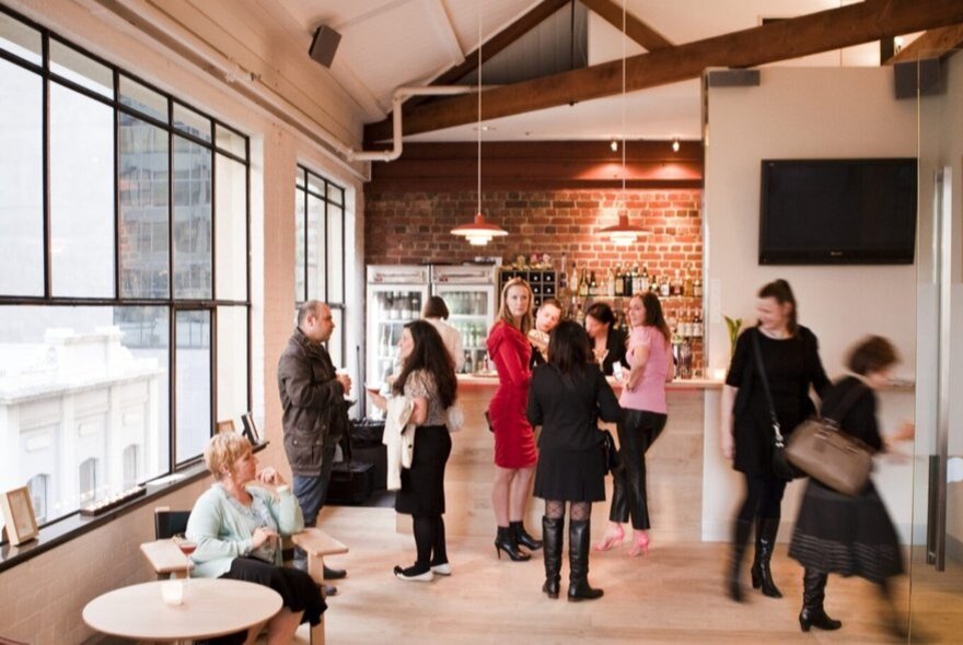 People seated and standing chatting in a bar area with pendant lights.