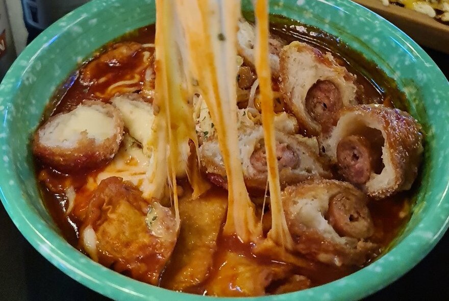 Close up of soup dish, in aqua bowl, with stretchy, glutinous noodles being pulled from soup.