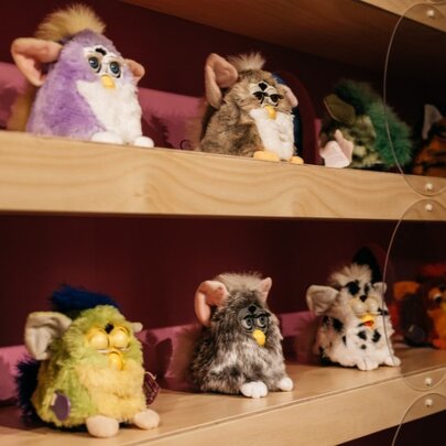 A collection of vintage Furby electronic robotic toys displayed on wooden shelves.