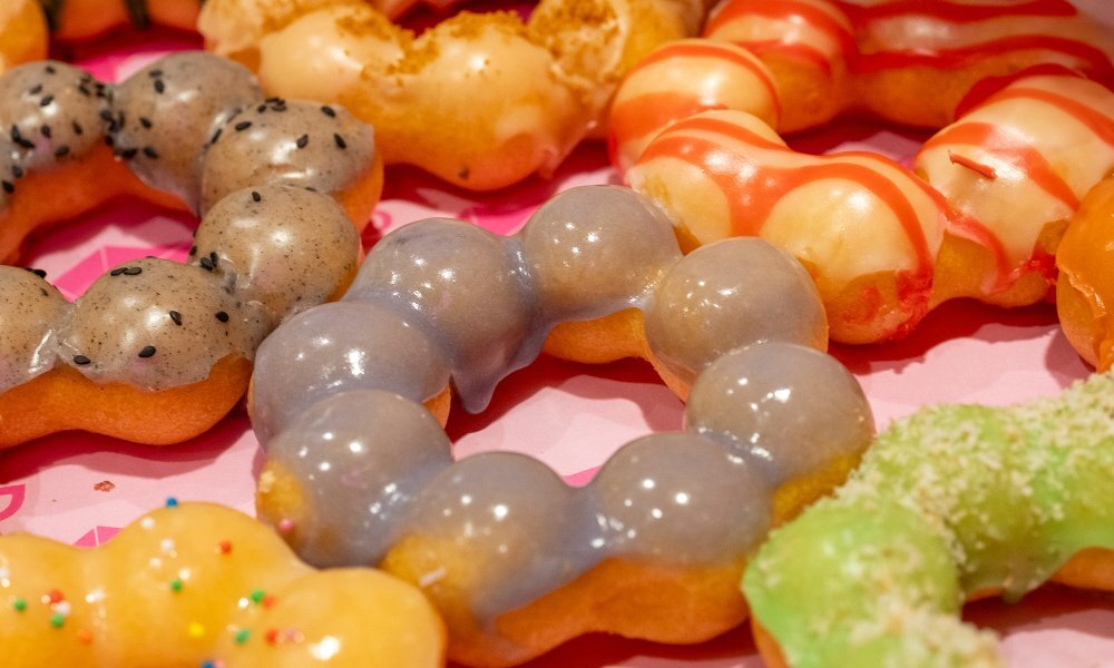 A tray of bobbly mochi doughnut rings covered in different coloured glazes.