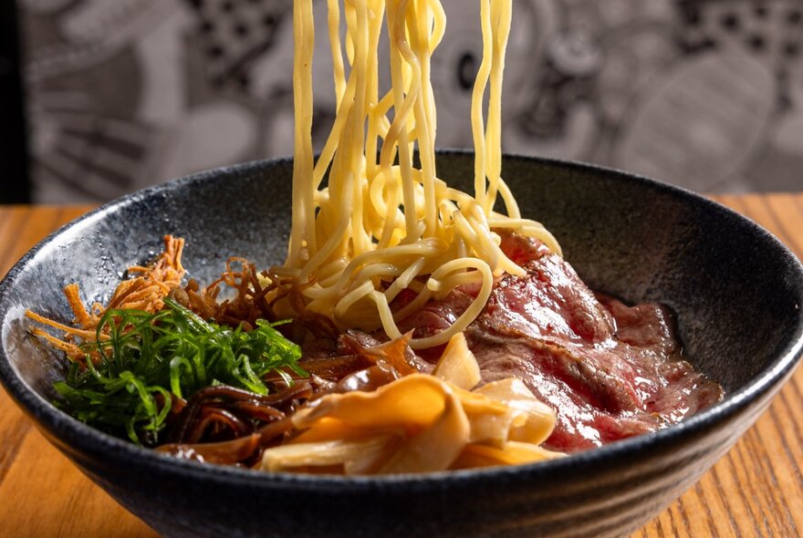 A bowl of ramen with vegetables, noodles, meat and broth.