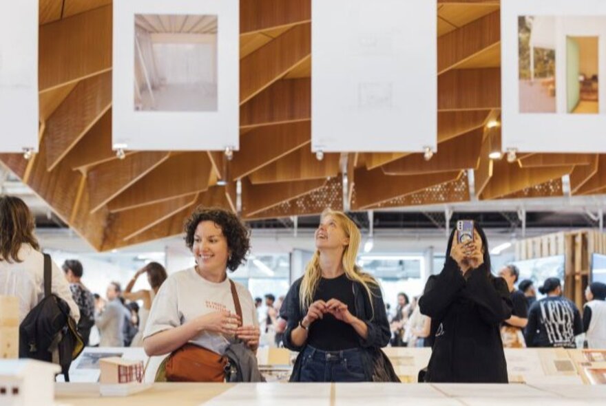 People looking at displays in an exhibition space with overhead installations and desks.
