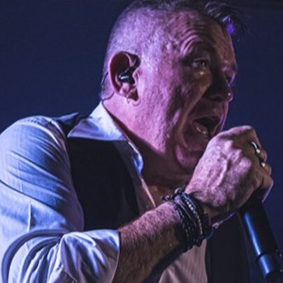 Cold Chisel tribute artist, Steve Cal, singing into a microphone and wearing a vest and white shirt.