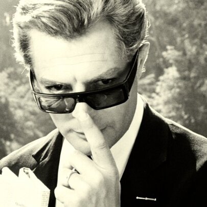 Actor Marcello Mastroianni in the 1963 film 8½, wearing a classic dark suit and sunglasses.