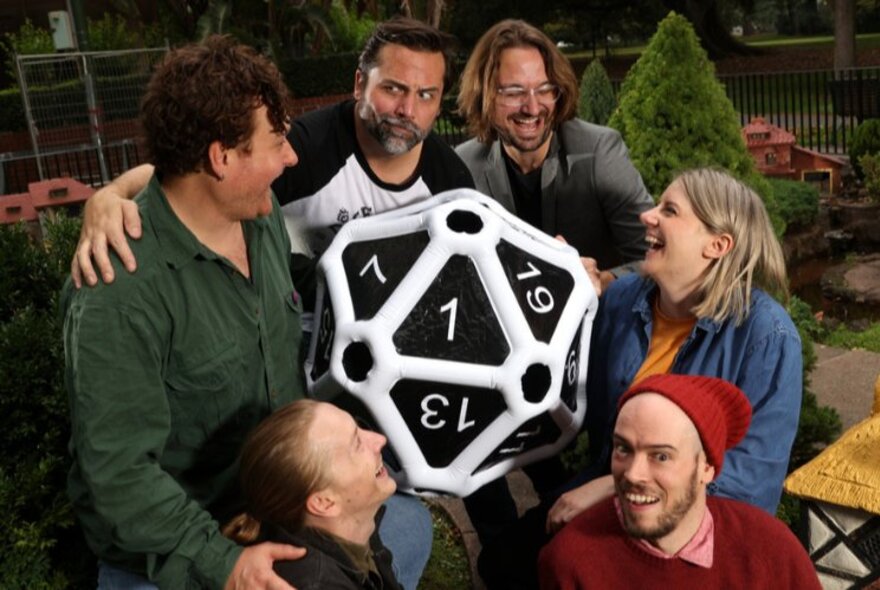 A group of people all laughing and posing around a very large multi-sided die.