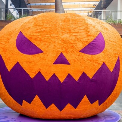 A large, orange inflatable Halloween jack-o'-lantern with a textured surface, a brown stem on top, and sharp, purple facial features of  triangular eyes and a jagged mouth.