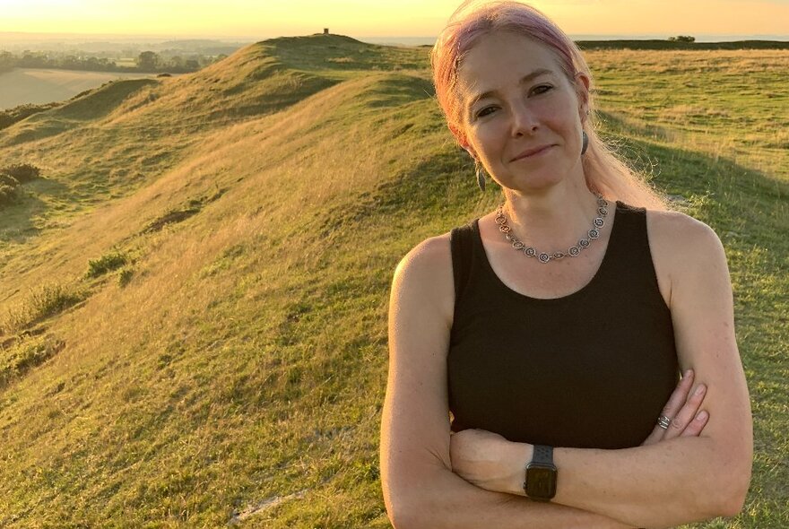 Professor Alice Roberts in front of a large mound in a grassy field.