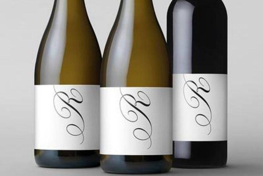 Three bottles of wine with a distinctive pale label with a large cursive letter R on its side, denoting the winemaker.