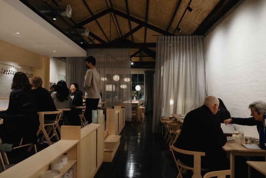 Interior of the restaurant Leonie Upstairs showing diners seated at tables, white walls, and long white curtains in the rear space.