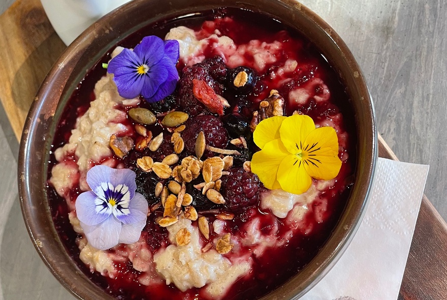 A bowl of breakfast porridge garnished with nuts, stewed fruits and flower petals.