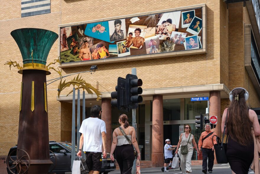 Brightly coloured artwork on the cream brick facade of the Hero Apartment building, with passers-by and a car on the road below.