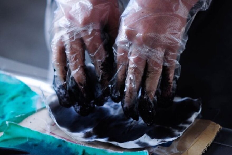 Hands wearing plastic gloves dyeing textiles.