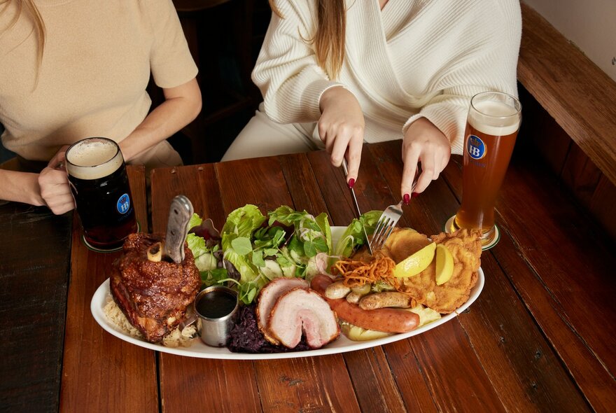 People seated at a table with jugs of beer and shared meat platter.