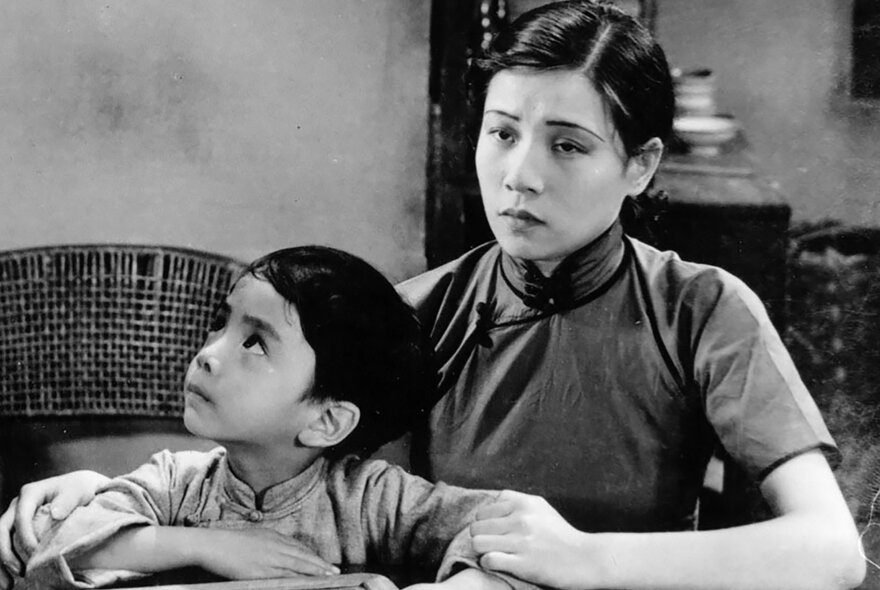 Black and white still from the silent Chinese Film, The Goddess, showing a sad young mother and her son in traditional Chinese clothing. 