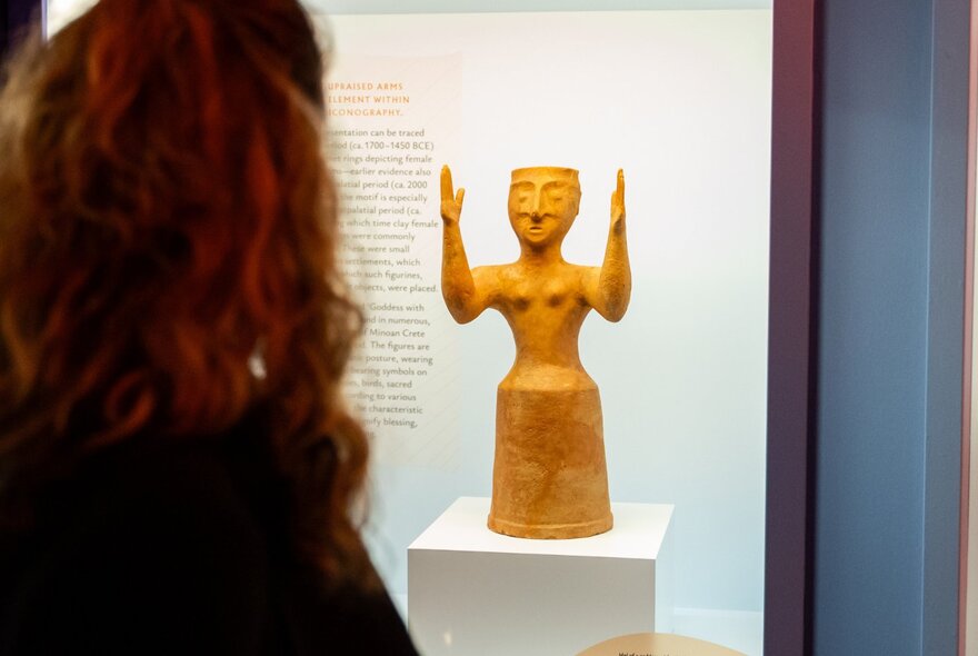 Person looking at a small ancient statue on display in a glass case at a museum.