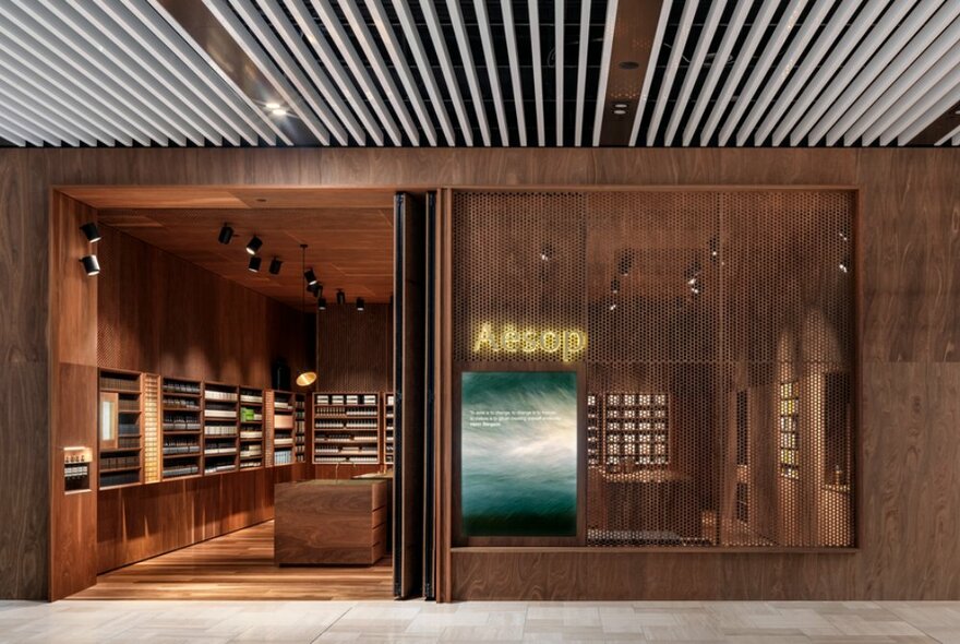 The warm wood exterior and interior of an Aesop shop with products on shelves visible through the door. 