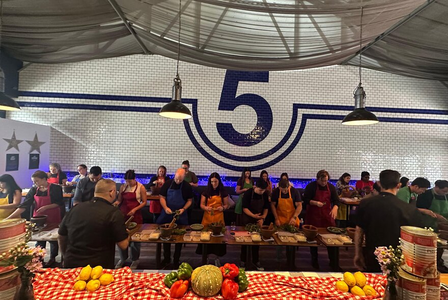 A group of people wearing aprons and standing behind a long wooden table as they participate in an Italian cooking class.