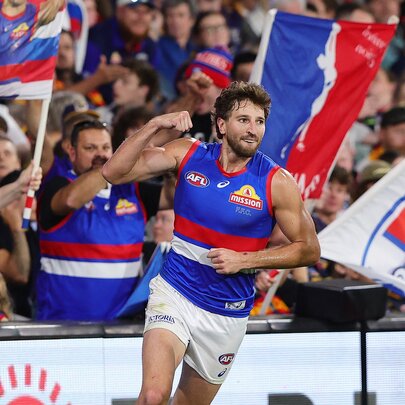 Western Bulldogs AFL football player shaking a fist as he runs past fans in the stands during a game.