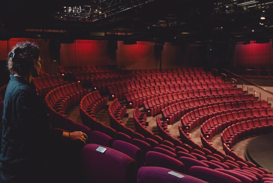 A behind the scenes tour of one of the theatres at Arts Centre Melbourne, with  person standing behind the last row of red theatre seats and looking towards the stage.