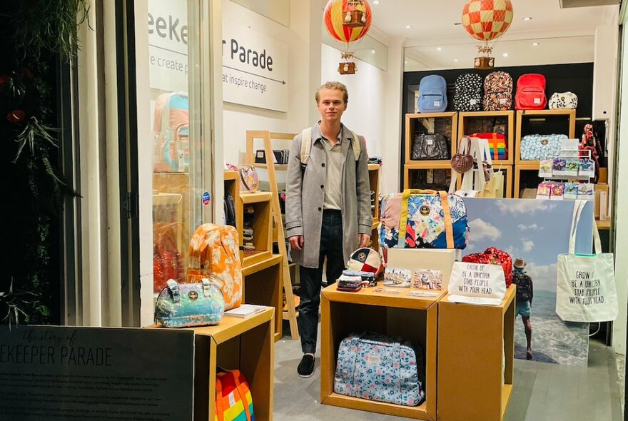 Person standing inside a retail space, with many products on display around them, on shelves and cabinets. 