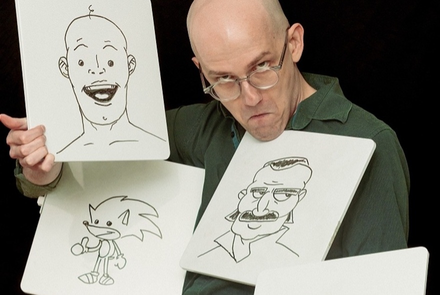 Zach Navarre  holding up drawings of people's faces and Sonic the Hedgehog, gripping one picture with his chin.