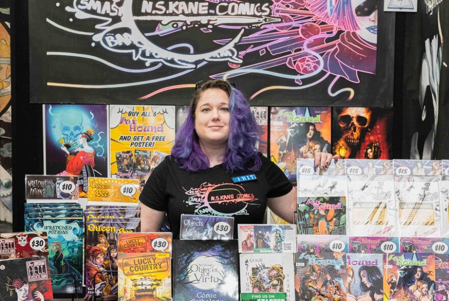 A woman with purple hair at a book stall showcasing all the books she has authored.