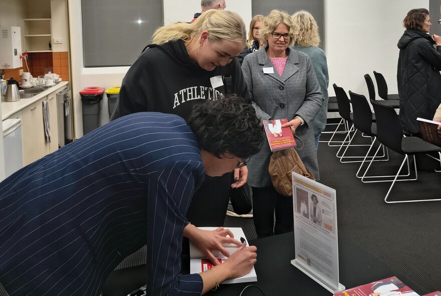 An author at a book talk signing copies of her book to people who are waiting in a queue.