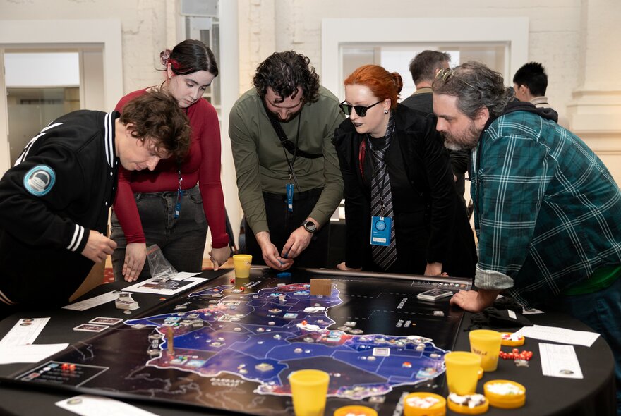A group of people standing over a game table playing a strategy board game.