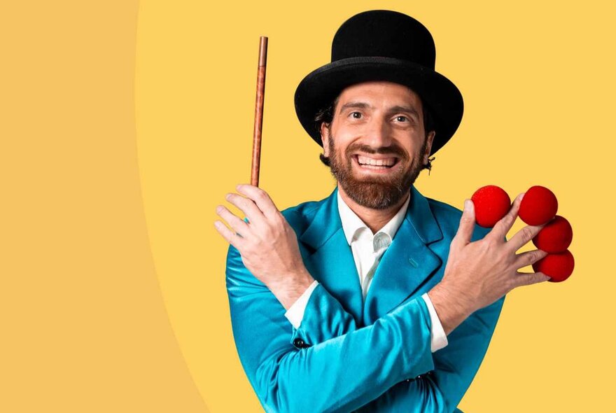 The Great Armando, a children's magician wearing a black top hat, a turquoise suit, holding a short wand in one hand and four red balls between his fingers in the other hand.