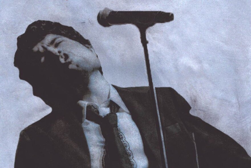 Singer Dhruv, wearing a suit with his head leaning back, singing in front of a microphone, black and white image.