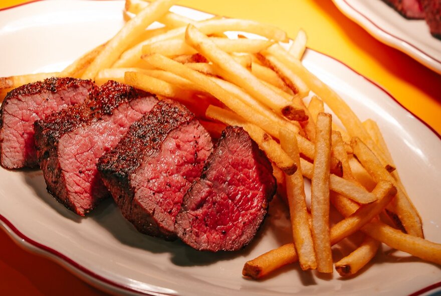 A white plate with a sliced steak and plenty of fries.