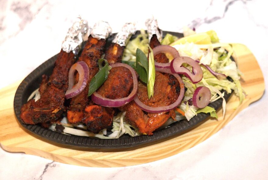 A dish of Tandoori chicken served on cast iron plate and wooden board.