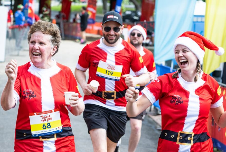 People jogging and smiling while participating in a fun run, all wearing Santa t-shirts.