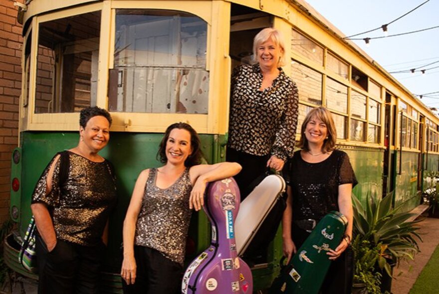 The four female members of the Flinders String Quartet posing in front of a vintage yellow and green Melbourne tram.
