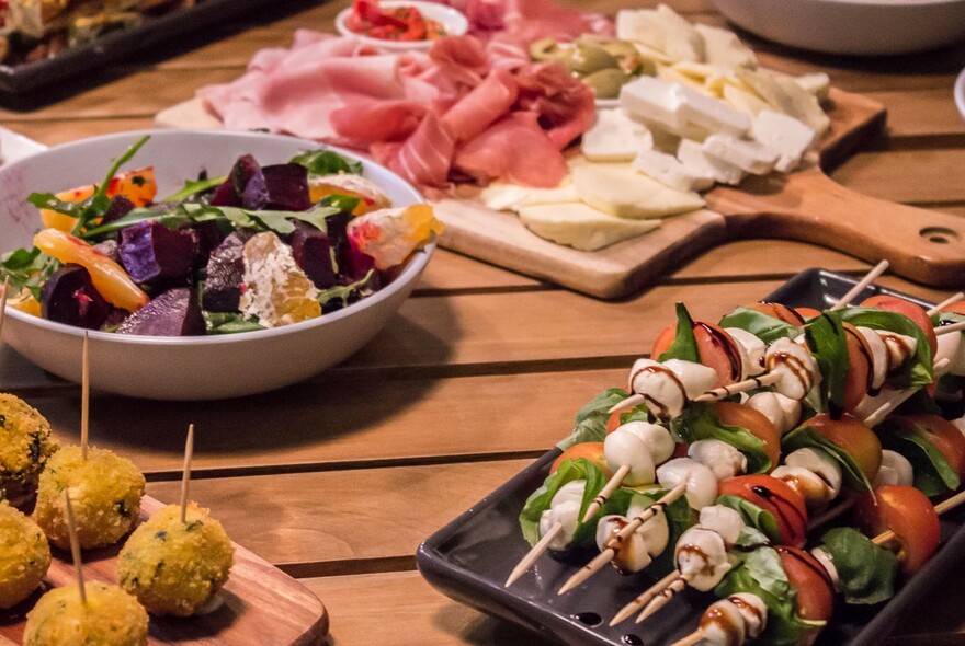 Table setting with platters of kebabs, appetisers, salad, cheese and charcuterie.